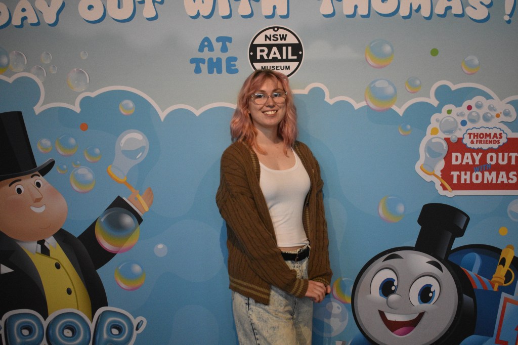 person posing in front of "Day Out With Thomas" poster